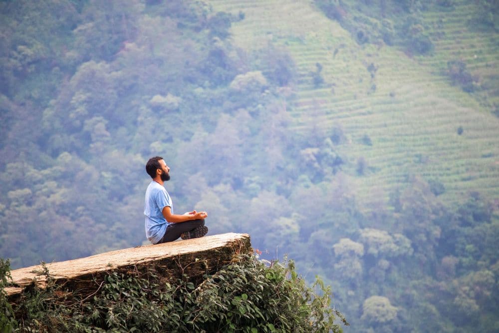 A man sitting in quiet reflection on a cliff edge overlooking a misty, terraced valley